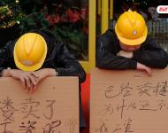 2012年12月25日，廣東中山，火炬開發(fā)區(qū)的多名建筑工人討要工作一年多的血汗錢一籌莫展，一些工人干脆將鋪蓋卷搬到了售樓部，并在門口搭起灶臺煮飯，希望以這種方式討回工錢。圖為在銷售中心門外，工人舉牌討薪。吳進/視覺中國